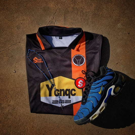 Camiseta YCNQC FC de SenliStudio en el suelo junto a unas Nike TN y un rosario, vista delantera